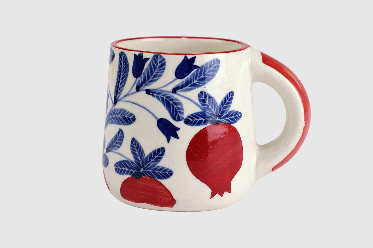 Ceramic mug with blue floral patterns and red pomegranate designs on a white background