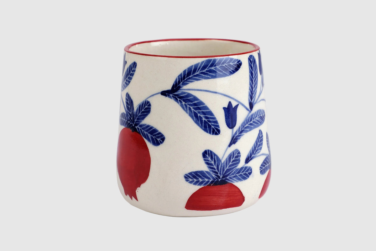 Ceramic mug with blue floral and red fruit design on a white background