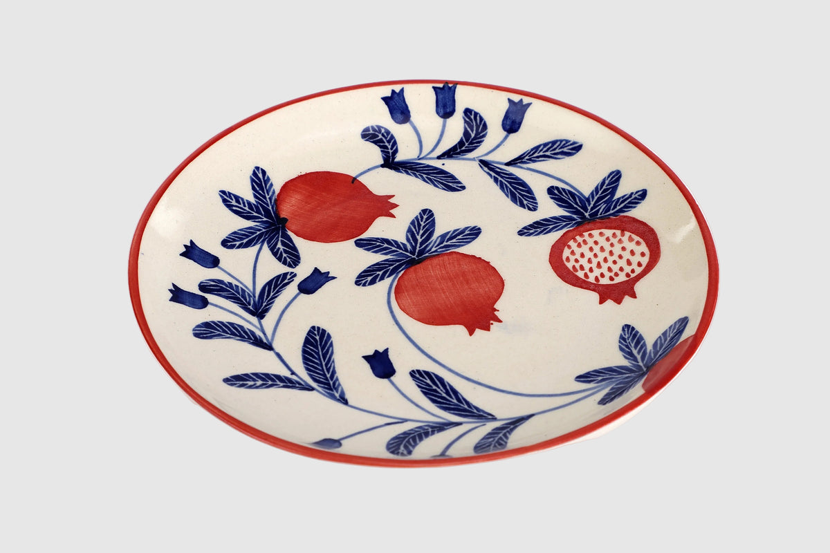 Ceramic plate with blue floral and red pomegranate design on a white background
