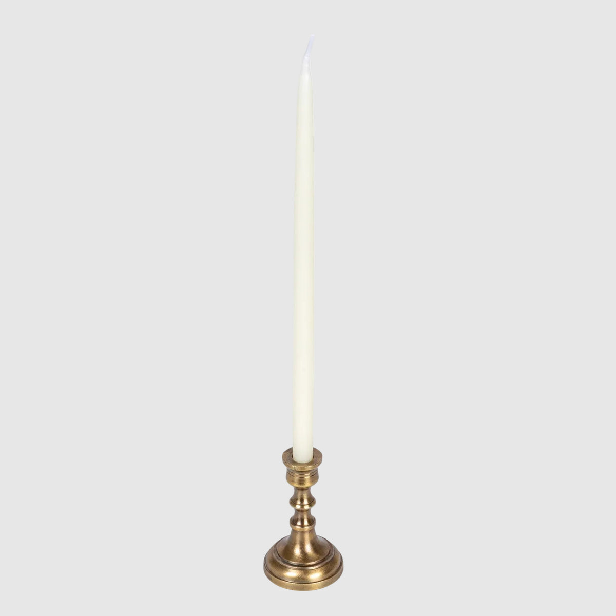 A single white taper candle in a polished brass or gold-toned metal holder, shown against a plain white background.