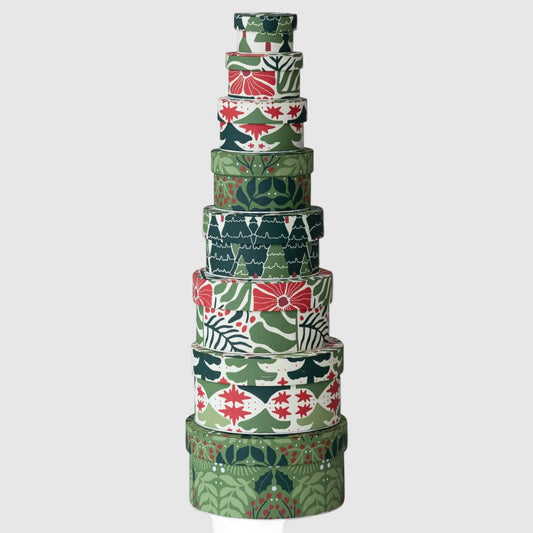 A stack of nine nested round gift boxes with festive Christmas patterns in green, red, and white, photographed on a clean white background.